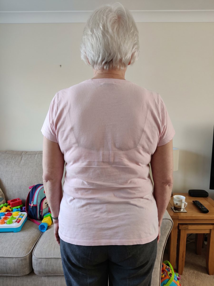 Ruth K. from behind in her usual bra: a band line and roll show through the top